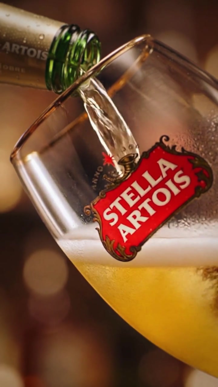 Garrafa de Stella Artois derramando cerveja em uma taça inclinada, com a marca vermelha em destaque.